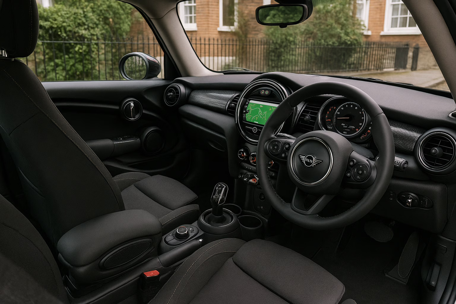 Interior of a modern Mini Cooper with black seats and dashboard, parked on a Chiswick residential street.